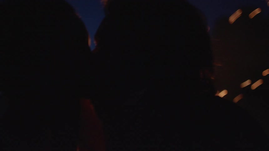 A man and a woman embracing and then kissing in front of a fire