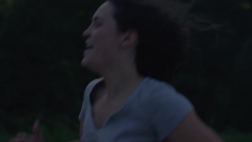 A woman pumps her arms as she runs past trees and fog