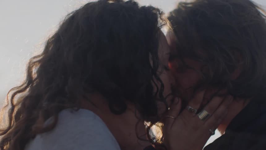 Man and woman kiss as they stand under a sunny sky