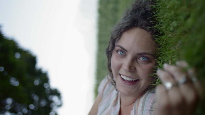 Young woman laying in grass looks at camera and laughs