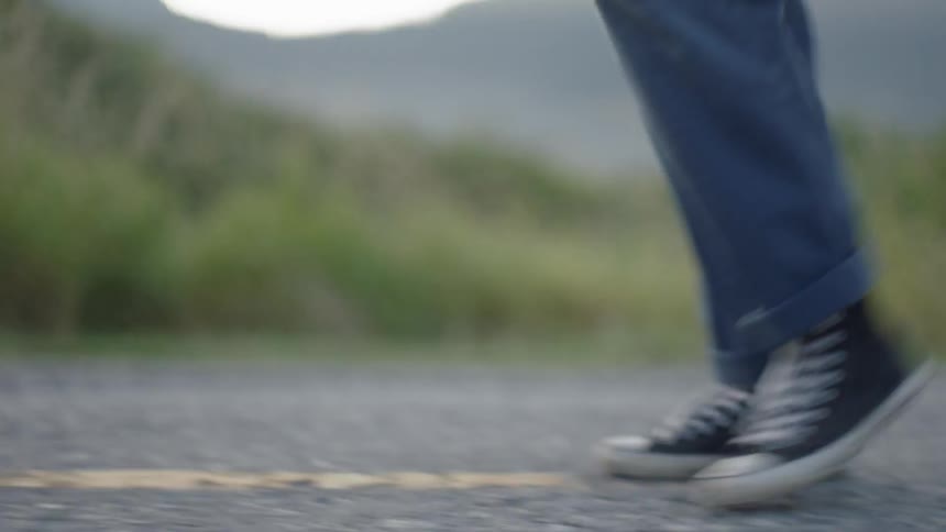 A person in blue jeans and converse sneakers walks on a rural road