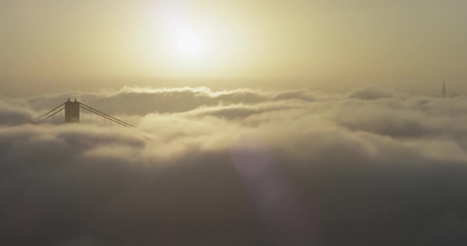 Cable bridge engulfed by clouds with the sun in the background