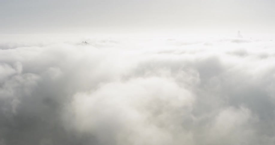 Antenna tower and mountain tops peek through clouds