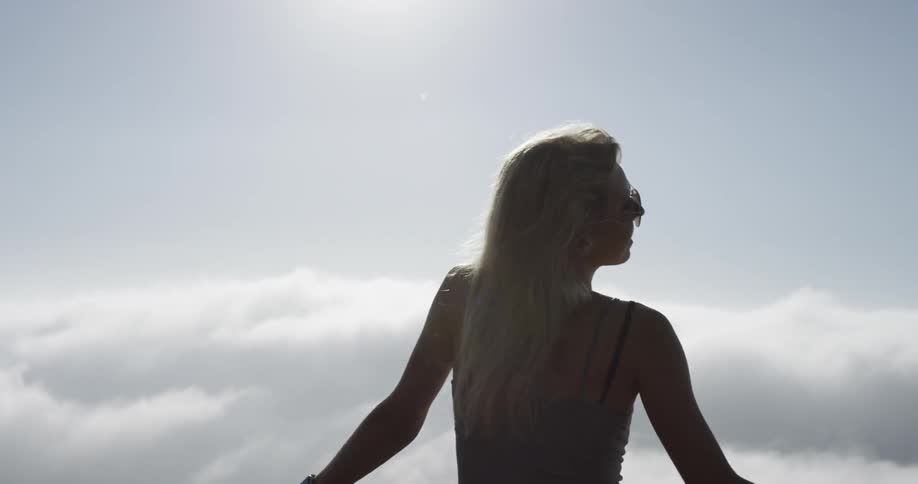 A woman stands at a fence and looks out at the fog and cloud covered bridge and scenic view