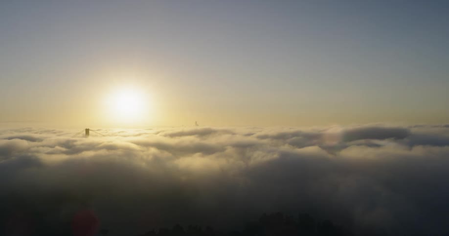 The sun above the clouds which hide a suspension bridge