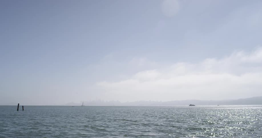 A body of ocean water is lined by distant mountains as two boats drift across the water on a sunny day