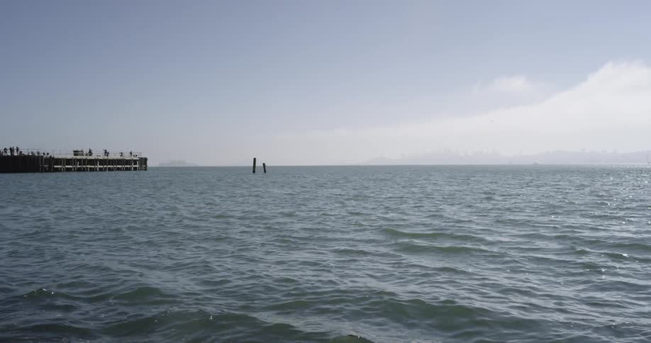 People walk on a pier which extends into a wide body of water