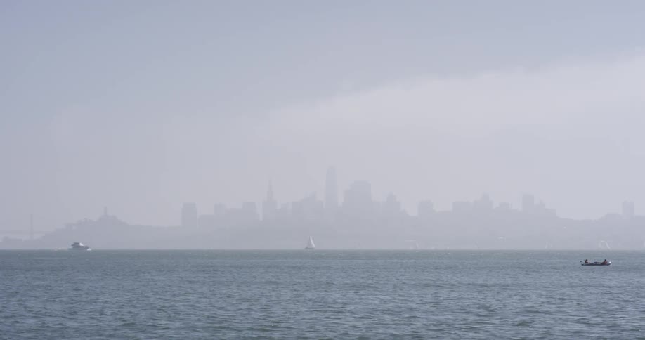 Boats sail across ocean near fog covered city