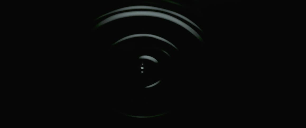 Water droplets fall one by one into a dark pool of water and send ripples out from the center