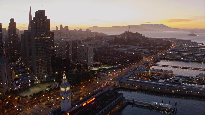 A coastal city skyline with docks and water during sunset