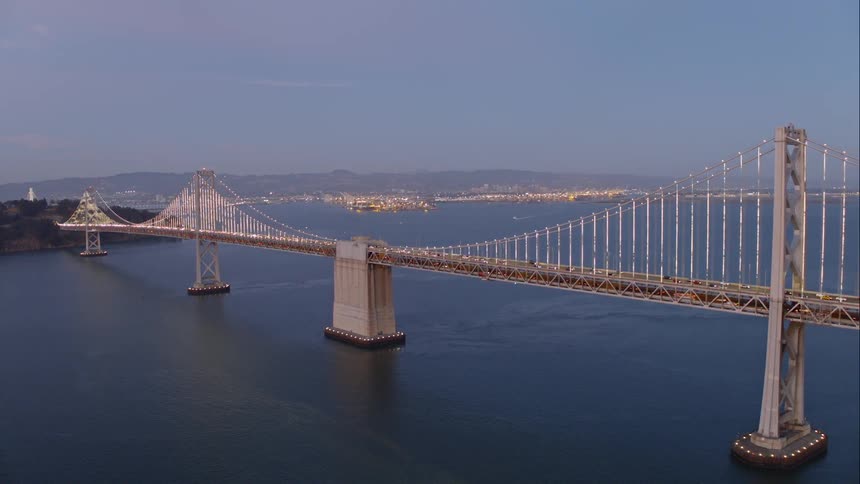 Traffictravels across a long bridge over water with town lights shining on the coast