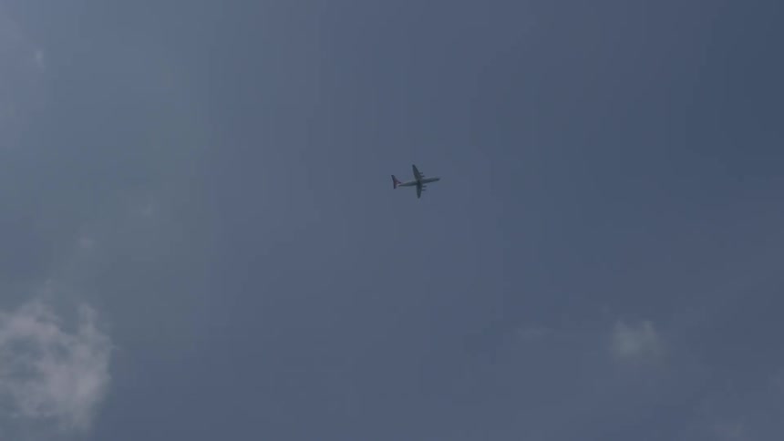 An airplane flies across the blue sky