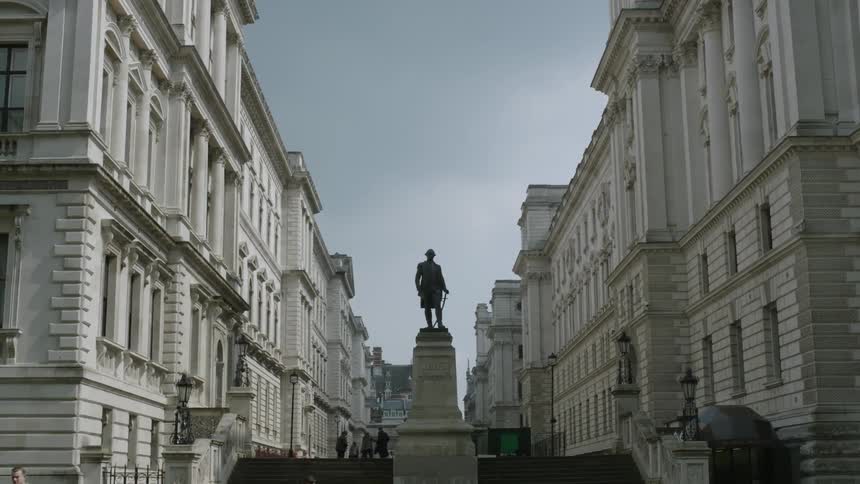 A group of people walk next to a statue between some buildings