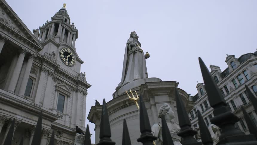 A large stone building has a clock tower at the top and a statue in front