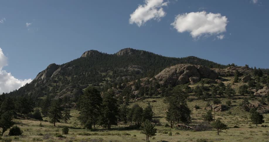 A rocky, tree covered hill under a few clouds
