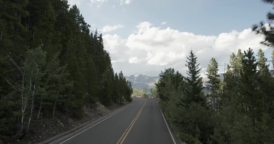 A large empty road has mountains in the distance on a cloudy day