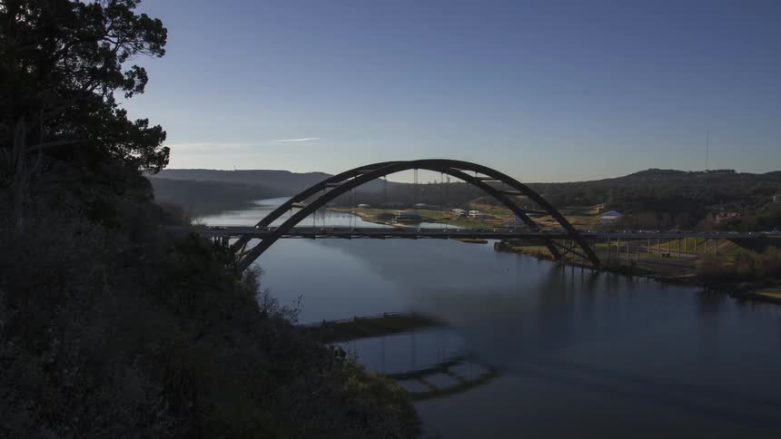Timelapse of daytime traffic crossing a bridge over a calm river