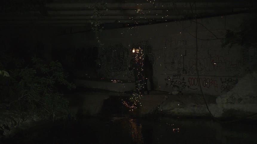 A silhouetted person swings a sparking object in the dark