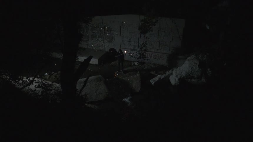 People standing on boulders in a very dark area as one of them waves a flare around in circles
