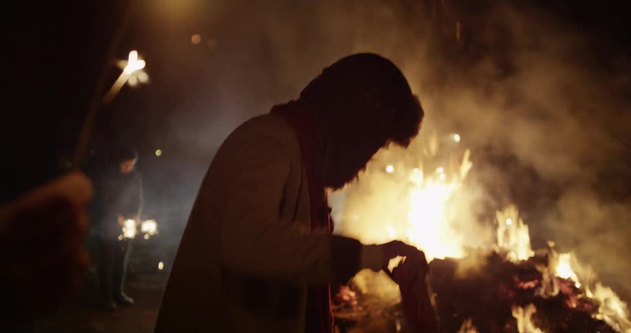 Group of people at night holding sparklers and dancing around a bonfire