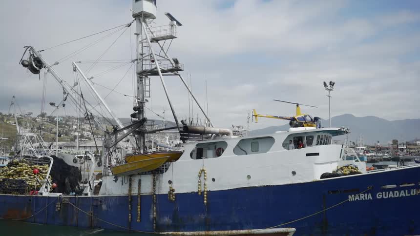 A helicopter with whirring blades sits on a landing pad on a large ship