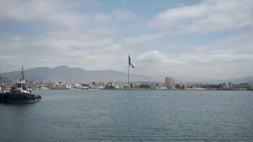 Commercial boats move across sea away from city with mountains on the horizon