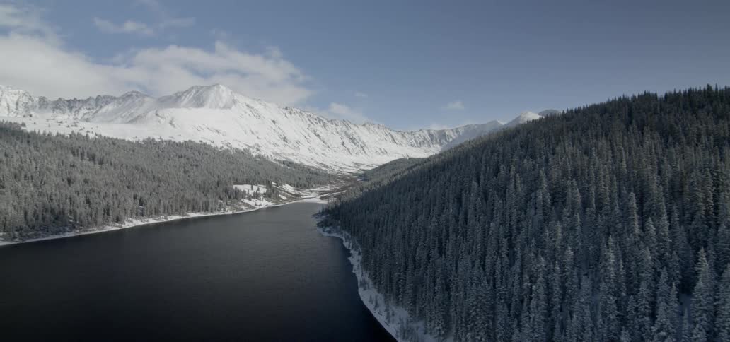 Forests line a mountain lake with a snow capped mountain against a blue sky