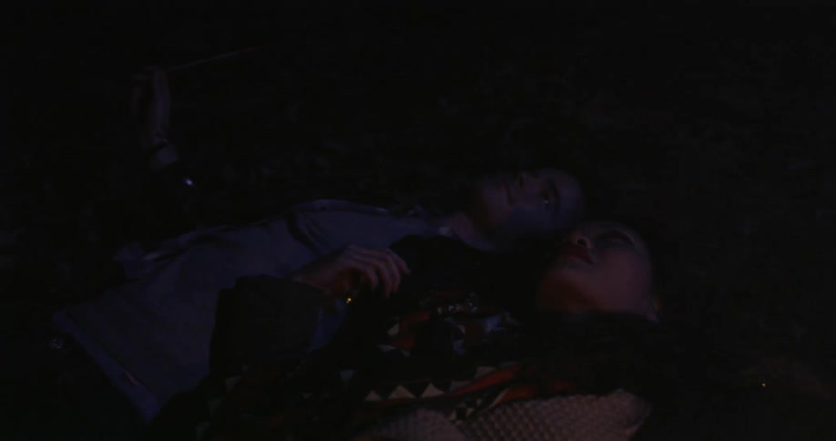 Man and woman laying on the ground holding sparklers and looking up at the sky,