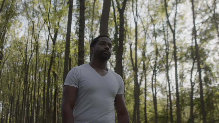 Black man wearing white t shirt walks in the forest during daylight