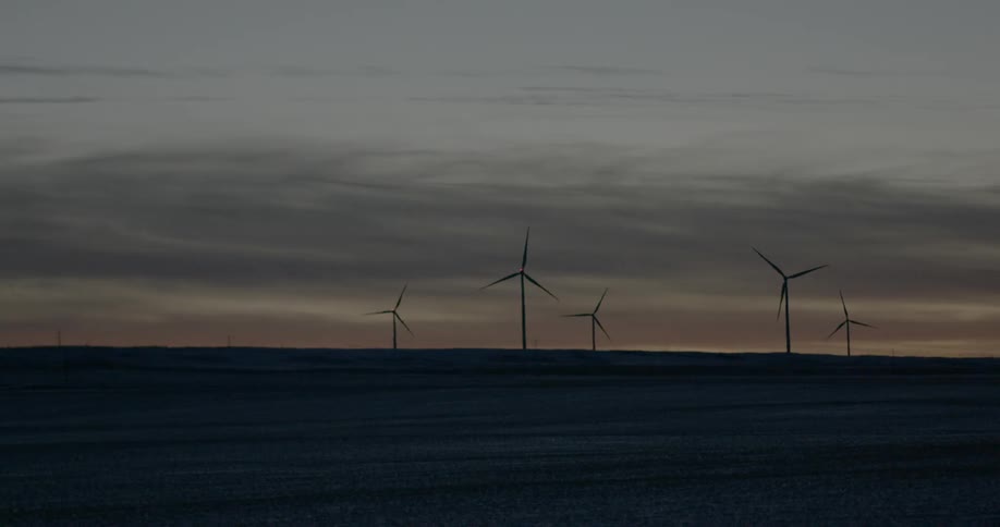 Several wind turbines on a barren landscape at sunset