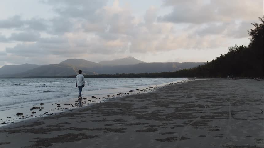 A man walking on the beach with the sky and mountains in the background