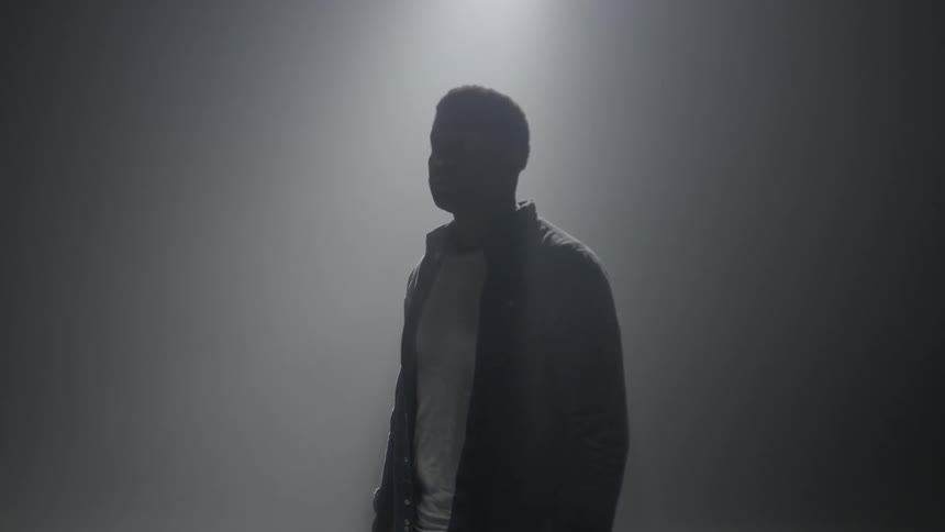 A black man stands in a smoky room