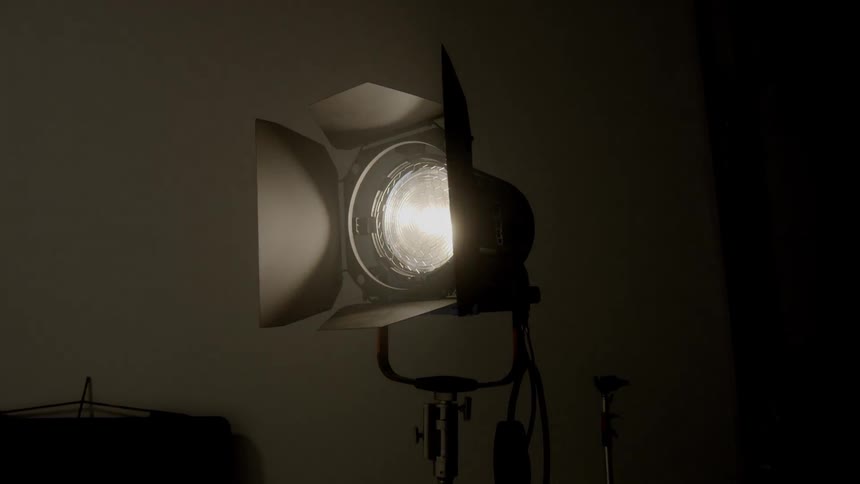 A studio light on a stand with directional shades turns on and illuminates its subject