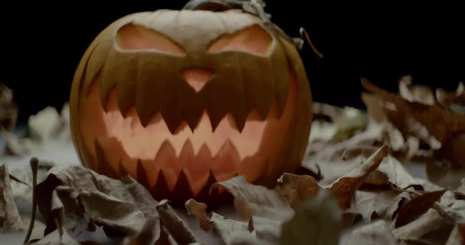 A glowing jack olantern sitting among dead leaves
