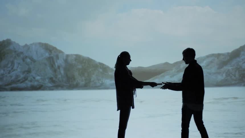 A woman walks over to a man standing in front of a large video screen and hands him an object