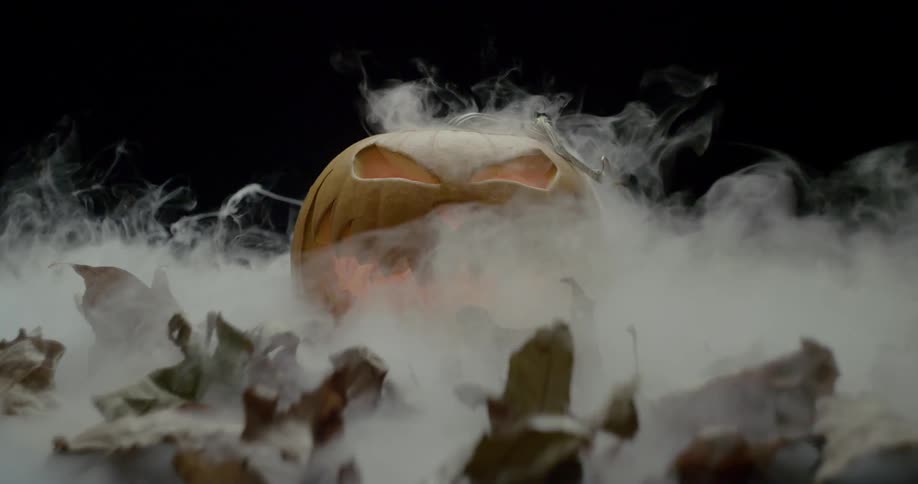 A jack olantern in a dark room surrounded by mist and leaves