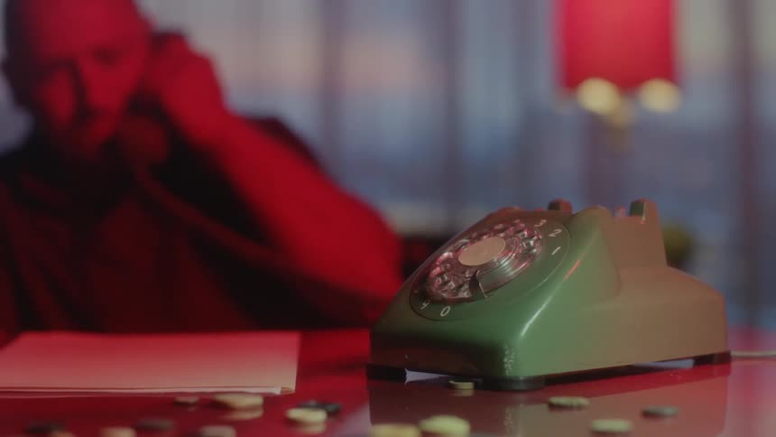A man sits at a desk and lifts up a surf green colored phone from its base and puts it to his ear before placing it back on its base