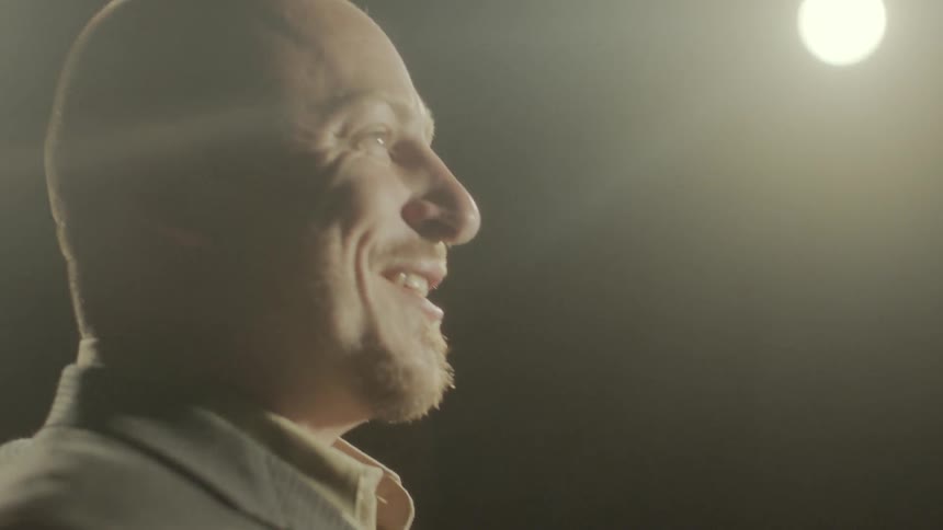 Man stands on a stage with stage lights around him and talks