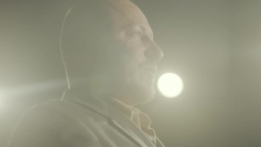 A man in a suit is speaking under spotlights in a dark environment