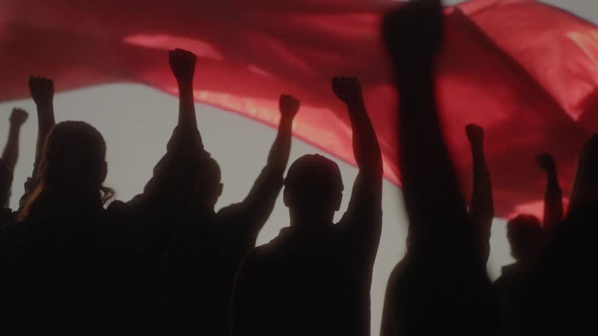 Group of people silhouette raise their fists in front of a red flag