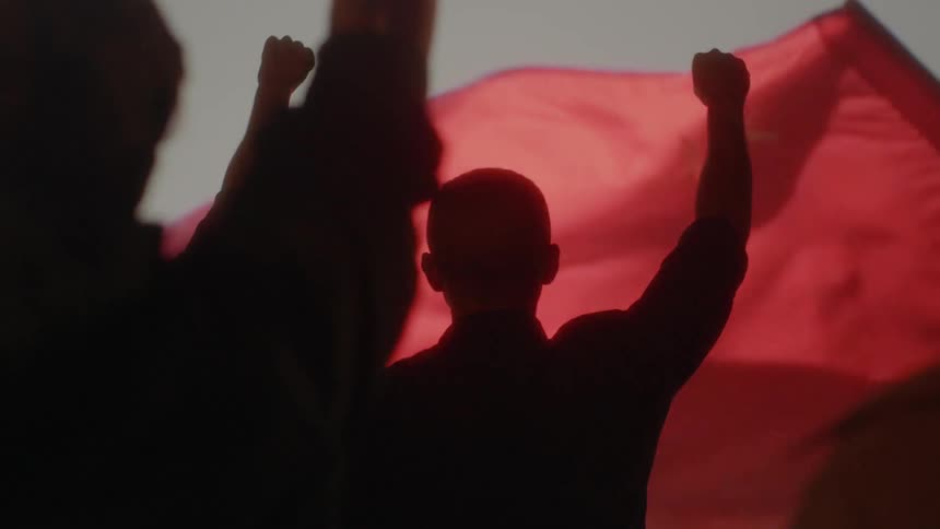 Men raise their right hands to a red flag which is flying in the wind
