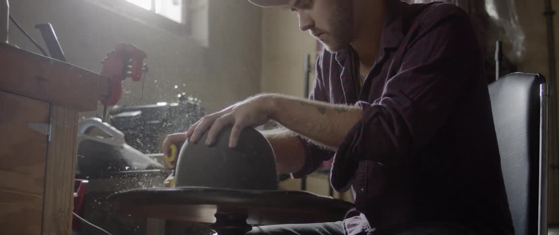 Man crafts felt hat using power tool in workshop