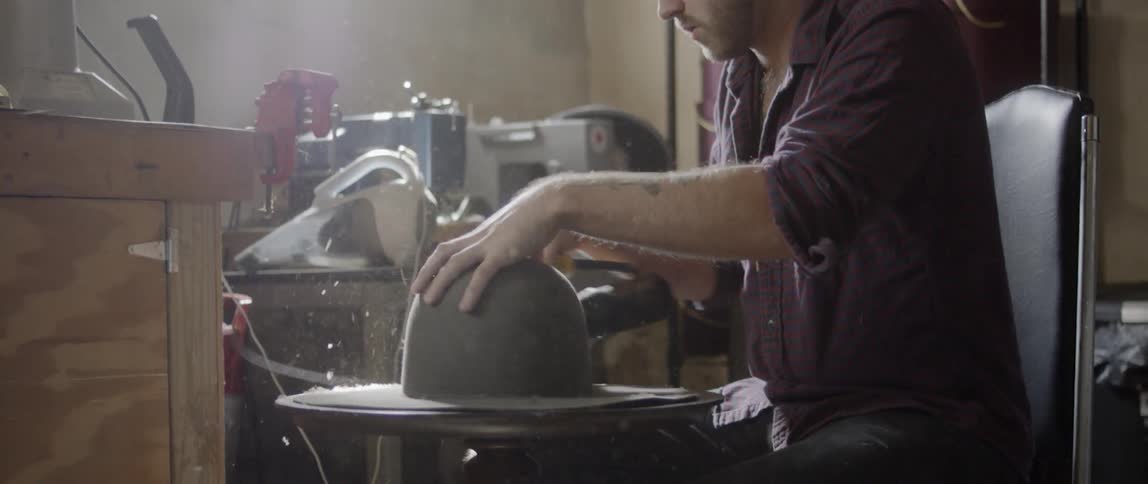 A man uses a sander on the rim of a hat