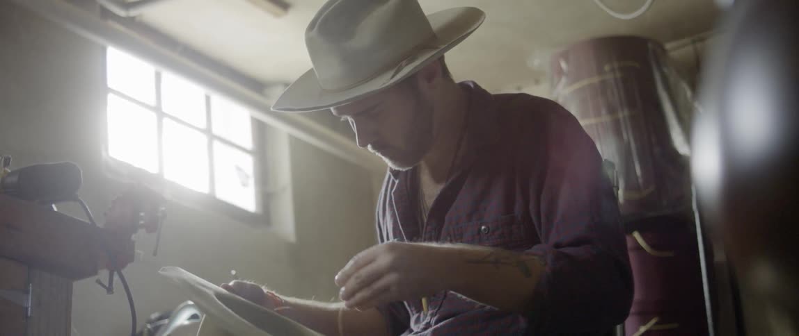A man stitching a cowboy hat in a barn or garage