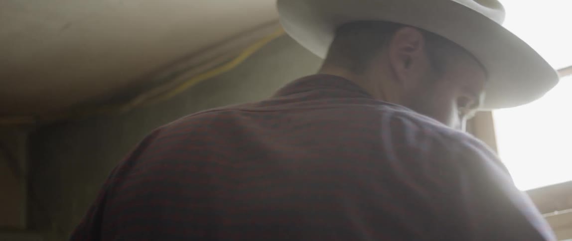 A man wearing a cowboy hat works indoors near a window