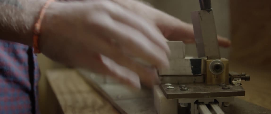 A man is using a machine to cut a leather strap