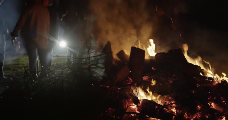 People are standing around at large campfire at night