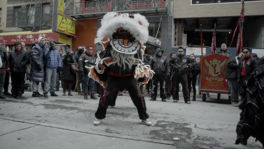 A pair of people performing a lion dance for a crowd in the streets