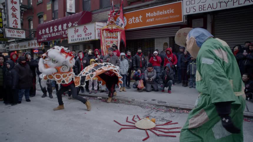 Asian people in costumes dance in a city street to entertain a crowd