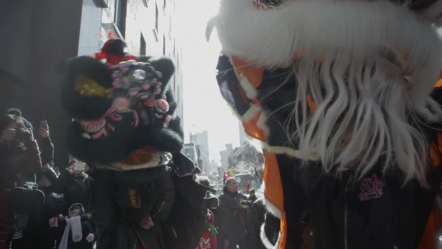 People stand on a street watching festival dancers in dragon costumes